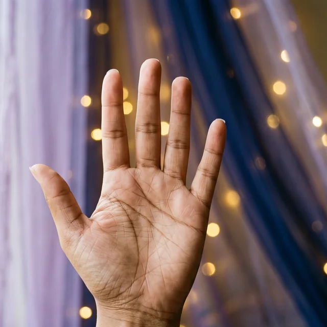 An open palm with detailed palm lines held up before sheer lavender and indigo drapes with golden lights