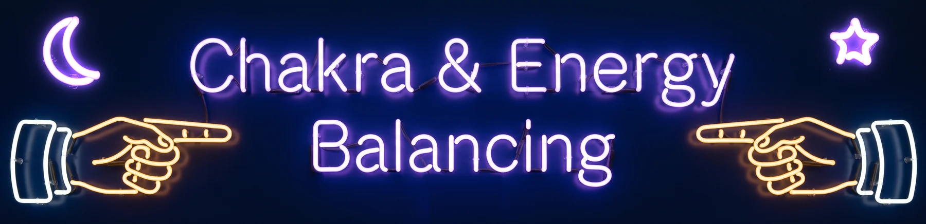 Neon sign reading Chakra & Energy Balancing, with two glowing hands pointing at it and a crescent moon and star in the top corners